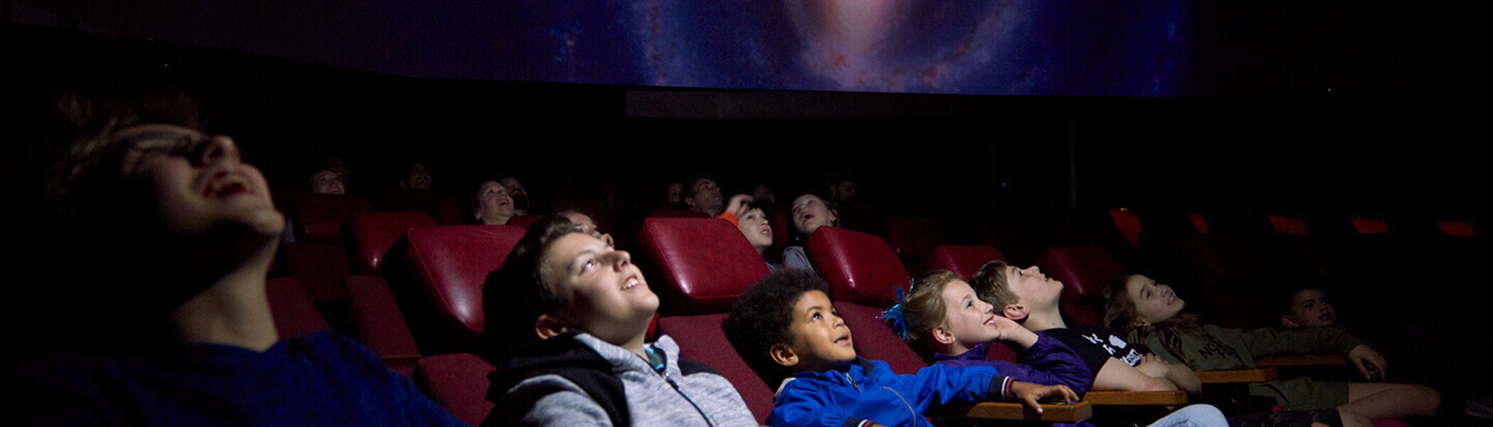 Children sitting in reclined seats smiling looking up at a screen